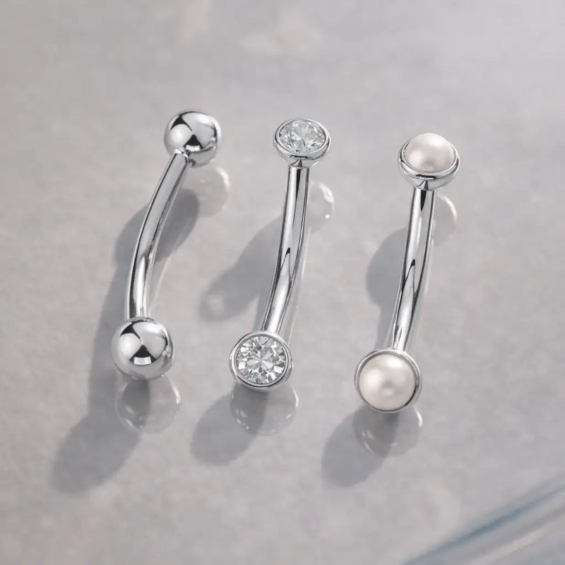 14k white gold curved barbells displayed with CZ bezel and pearl end styles on gray surface