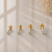 Four 14k yellow gold diamond flat back labret studs in graduated sizes displayed on warm stone surface