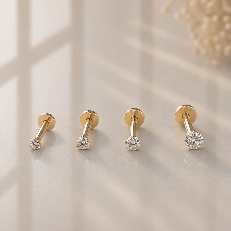 Four 14k yellow gold diamond flat back labret studs in graduated sizes displayed on warm stone surface