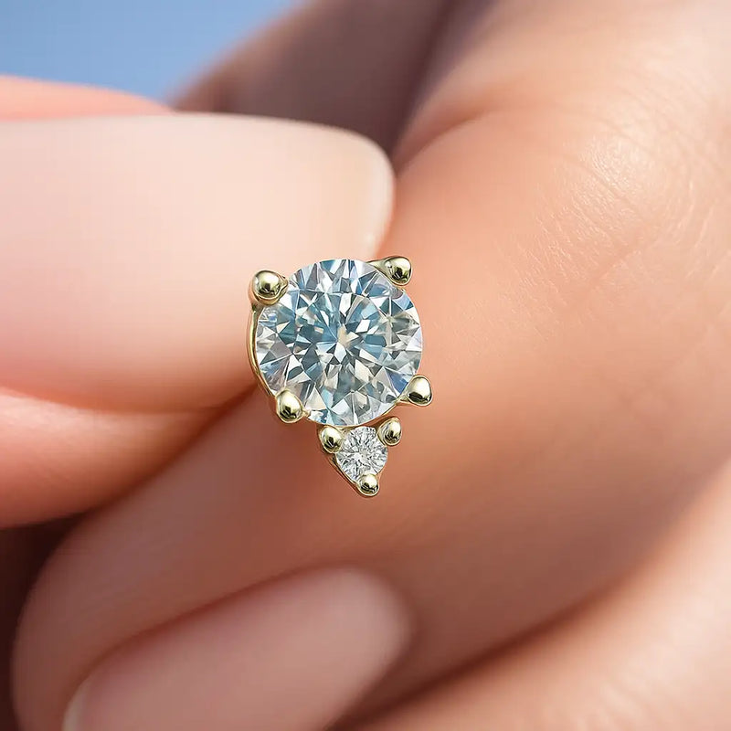Close-up of 14k yellow gold flat back labret top pinched between fingers, aqua gemstone and diamond prong detail