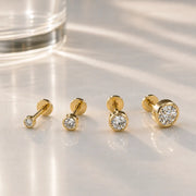 Four 14k yellow gold diamond bezel flat back studs in graduating sizes displayed on marble surface