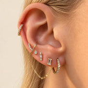 Curated gold ear stack with diamond stud ends and a draped connecting chain, shown on a model