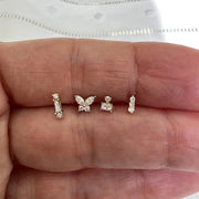 Diamond butterfly flat back stud shown alongside three other gold piercing studs for size comparison in hand