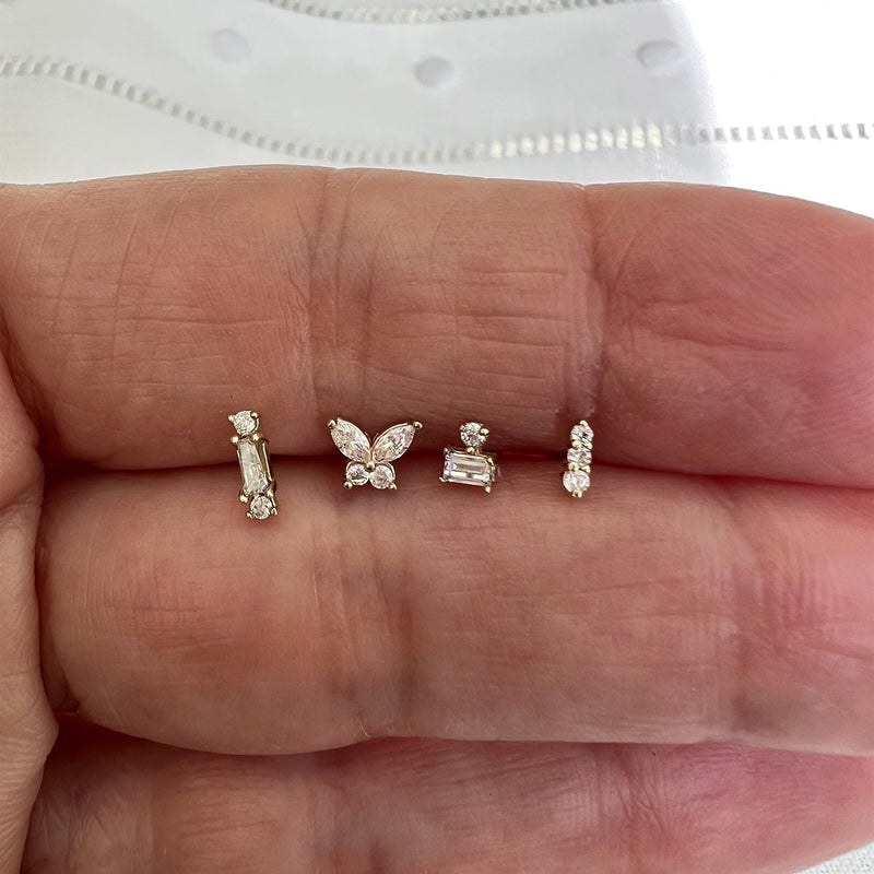 Diamond butterfly flat back stud shown alongside three other gold piercing studs for size comparison in hand