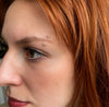 Model wearing a 2mm prong-set curved barbell in an eyebrow piercing, set in 14k gold