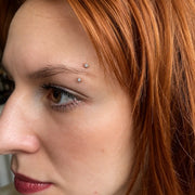 Model wearing a 14k gold prong-set curved barbell with 3mm clear gems in an eyebrow piercing - shown for size and placement; the ruby version is the same size