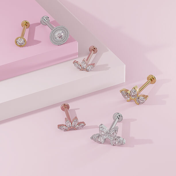 Marquise diamond fan flat back studs in rose, yellow, and white gold arranged on a pink display surface