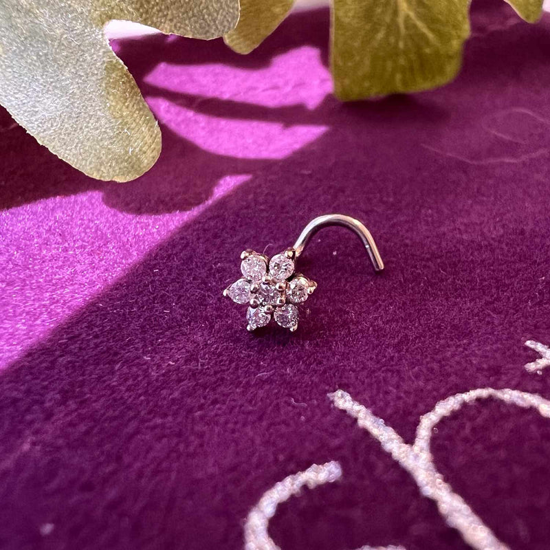 14K rose gold clear CZ flower nose ring twist resting on purple velvet with foliage backdrop