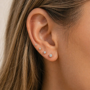 Close-up of an ear wearing different sized diamond stud earrings.