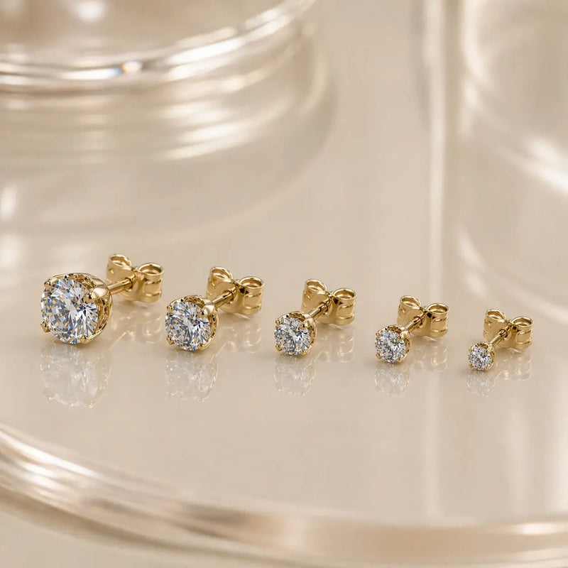 High-set diamond studs in various sizes displayed on a glass surface