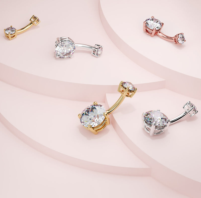 Diamond navel rings in 14k yellow, white, and rose gold shown together on pink surface