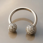 14K white gold diamond pavé circular barbell resting on reflective gray surface, angled view