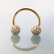 14K yellow gold circular barbell with diamond pavé balls standing upright on reflective surface