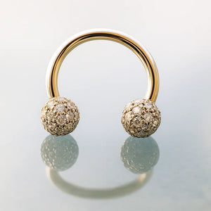 14K yellow gold circular barbell with diamond pavé balls standing upright on reflective surface