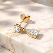 Diamond Pear Drop Stud Earring in 14K yellow gold resting on marble, round diamond solitaire with pear-shaped diamond drop