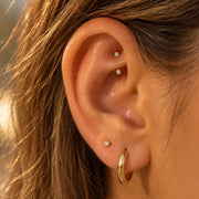 Rook piercing with a 2mm prong-set curved barbell, plus a stud and a thick gold hoop in the lobe, on a model's ear - diamond or cubic zirconia