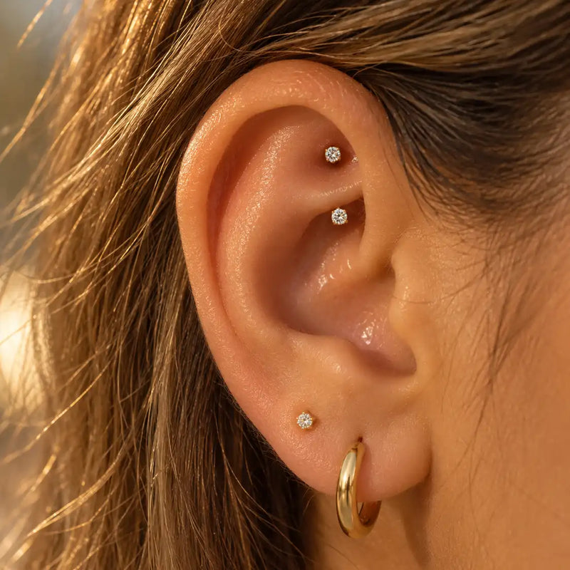Model wearing a 14k gold prong-set curved barbell with 3mm clear gems in a rook piercing - shown for size and placement; the ruby version is the same size