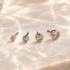 Four round bezel threadless ends with clear gemstones in white gold, yellow gold, and rose gold settings, arranged in ascending size order on a light beige marble surface.