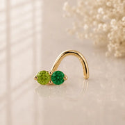 Emerald and Peridot double gemstone nose ring in yellow gold on a reflective surface lifestyle image.