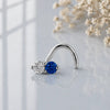 Diamond and blue sapphire, white gold, nose twist on a reflective surface with flowers in the background.