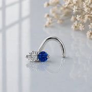 Diamond and blue sapphire, white gold, nose twist on a reflective surface with flowers in the background.