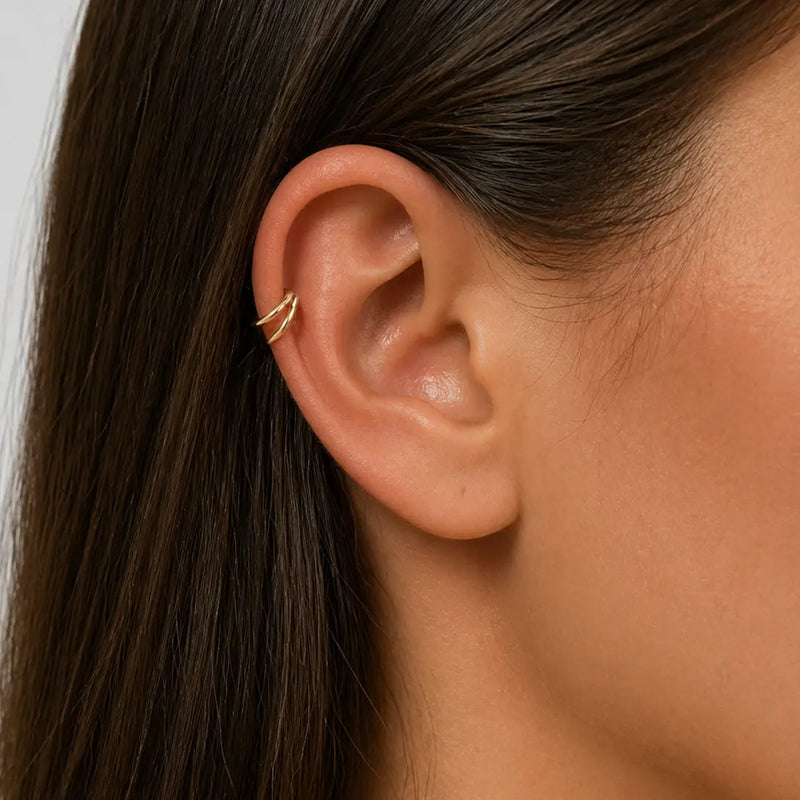 Close-up of an ear with a double hoop gold seam ring helix earring against a neutral background