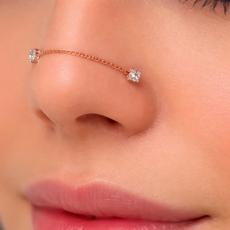 Rose gold duo gem chain connector shown on nose, linking two nostril piercings with CZ studs