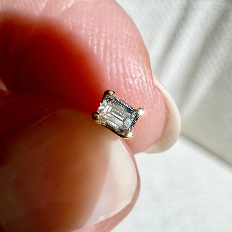 3mm emerald-cut diamond flat back stud pinched between fingertips showing true tiny scale of the piece