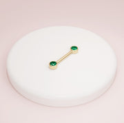 14K yellow gold emerald bezel nipple barbell resting on white ceramic tray, lifestyle shot