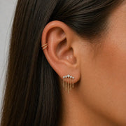Close-up of an ear wearing a gold earring with small stones and dangling chains with a gold double hoop helix piercing.