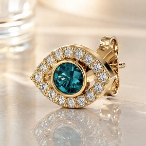 14k yellow gold evil eye stud earring with blue topaz center and diamond halo, lifestyle shot on reflective surface