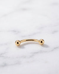 Curved barbells - plain 14k yellow gold curved barbell on white marble
