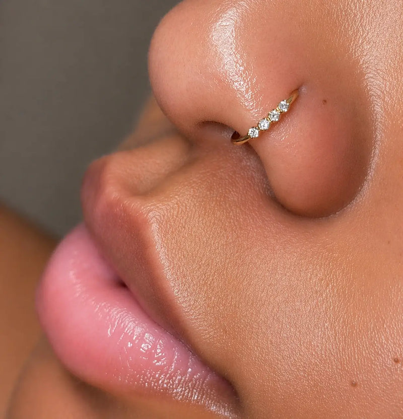 Macro close-up of four side-set diamonds on 14K gold seam ring worn in nose piercing
