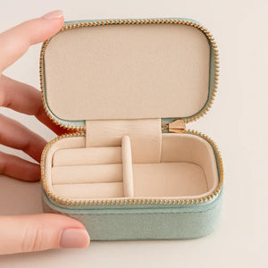 Open mint green travel jewelry box showing cream velvet interior with ring rolls, held in hands