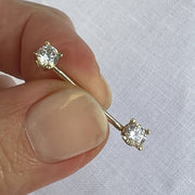14k yellow gold CZ straight barbell held between fingers for size reference
