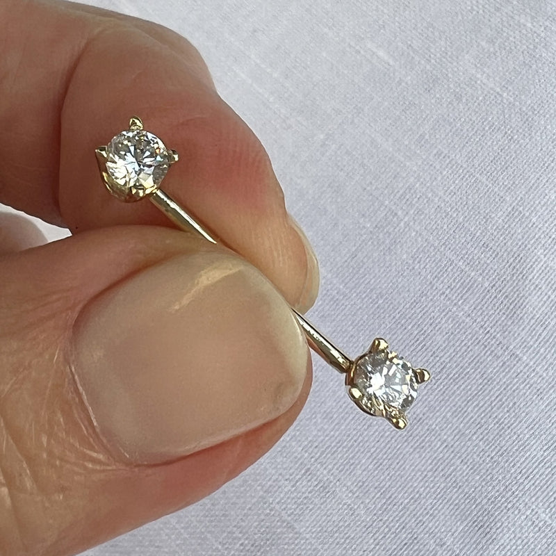 14k yellow gold CZ straight barbell held between fingers for size reference