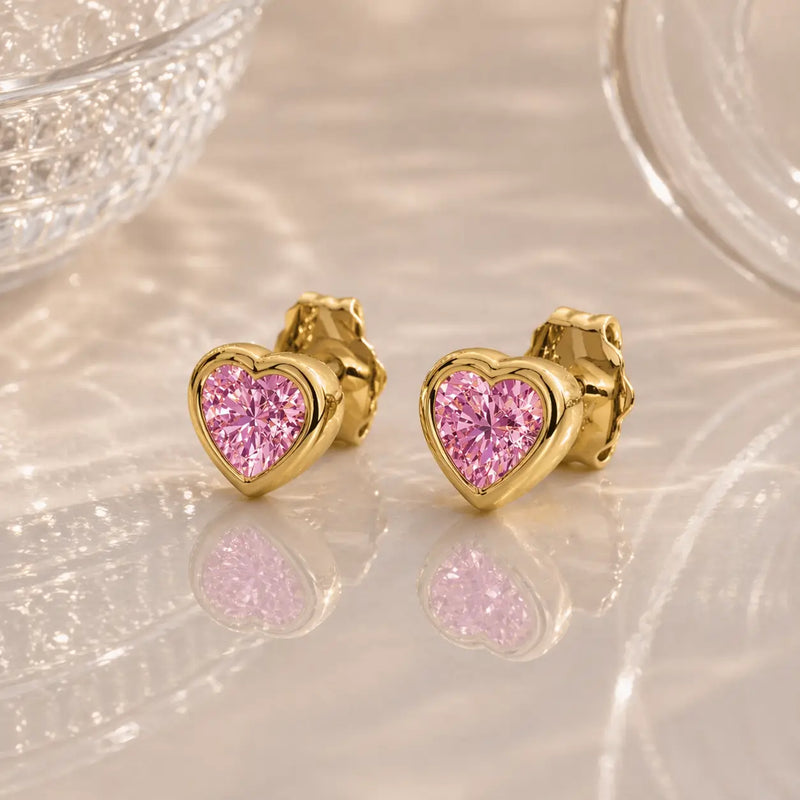 14k yellow gold pink sapphire heart stud earrings pair, bezel-set bright pink stones on soft background