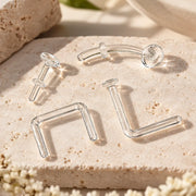 Four clear glass piercing retainers on travertine - flat back labret, curved barbell, septum staple and nose L-bend styles