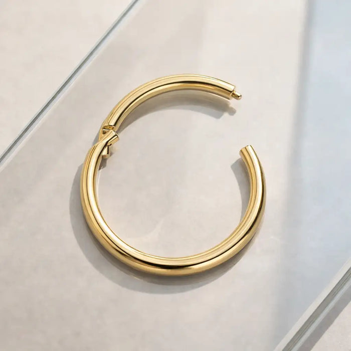 18K yellow gold clicker ring hoop shown open on marble surface, revealing hinged clicker mechanism