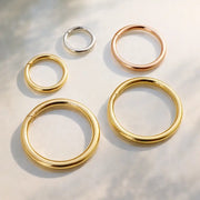 18K yellow, white, and rose gold plain clicker hoops in multiple sizes arranged on light surface