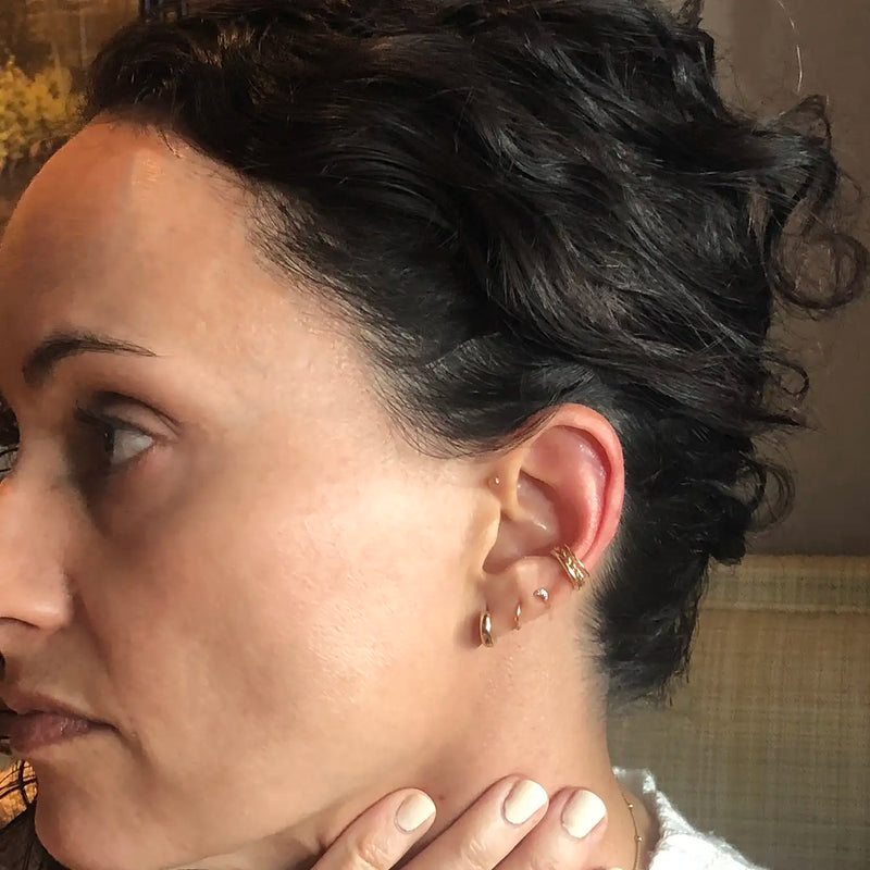 Model with short hair wearing layered 14k gold ear cuffs and small hoops, side profile
