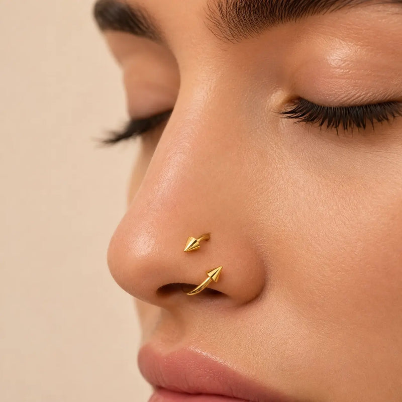 Close-up of a model's nose wearing a spiked spiral barbell against a soft beige background.