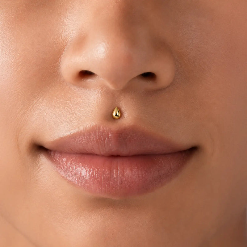 Model close-up of an woman's nose with a solid gold droplet flat back labret stud in her medusa piercing.