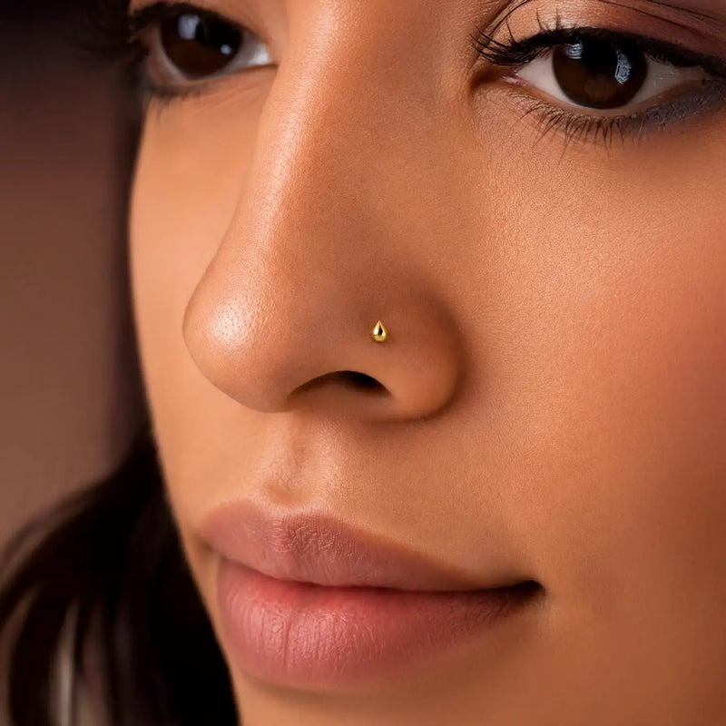 Close-up of a woman's face with a gold droplet stud nose ring.