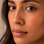 Close-up of a woman's face wearing a 14k gold droplet stud nose ring with a neutral background