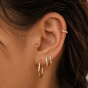 Close-up of a person's ear showcasing multiple gold cartilage piercings and hoop earrings.