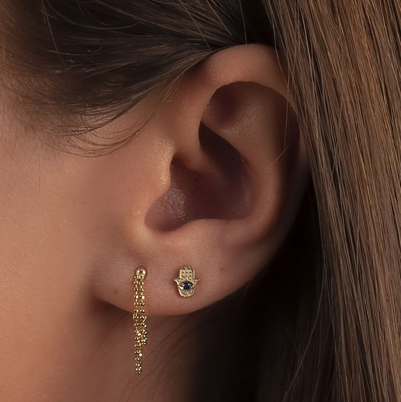 14k gold sapphire Hamsa evil eye stud shown in model's earlobe piercing for size and fit reference