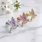 Hummingbird flat back earrings in 14K white, rose, and yellow gold with gemstones beside spring blossoms