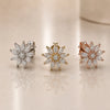 Three diamond earrings in white gold, gold, and rose gold on a reflective surface.