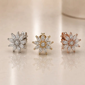 Three diamond earrings in white gold, gold, and rose gold on a reflective surface.
